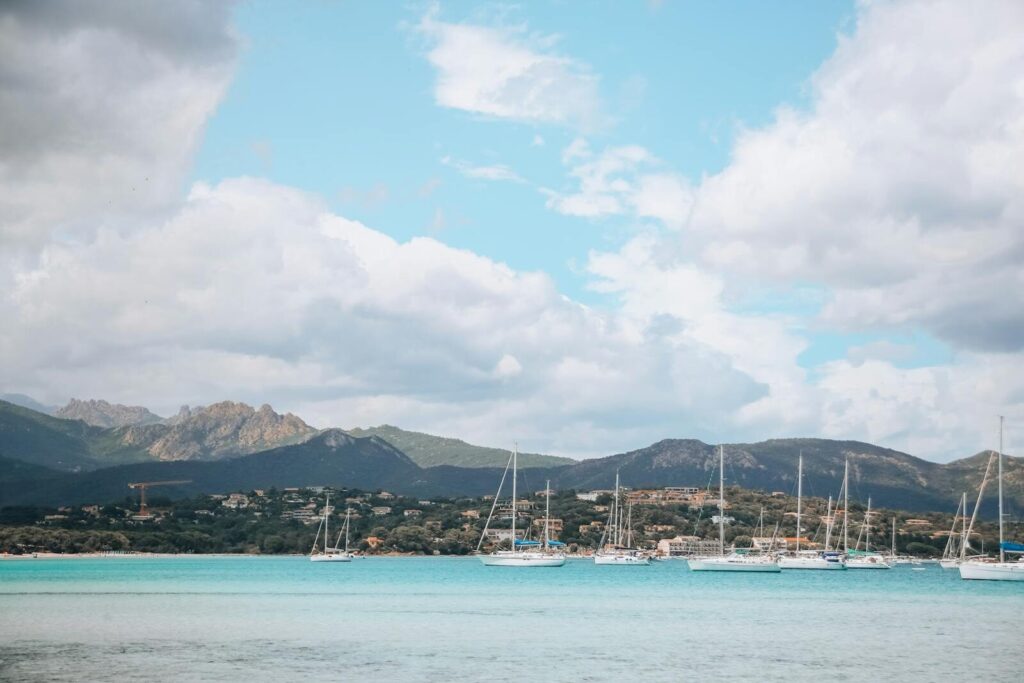 Scenic view of sailboats anchored in a serene bay with mountains and cloudy sky in France.