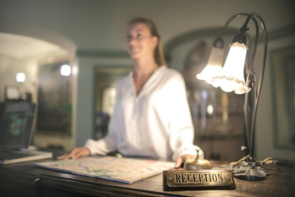 Blurred female in white shirt standing at reception desk with map on table and smiling while looking away